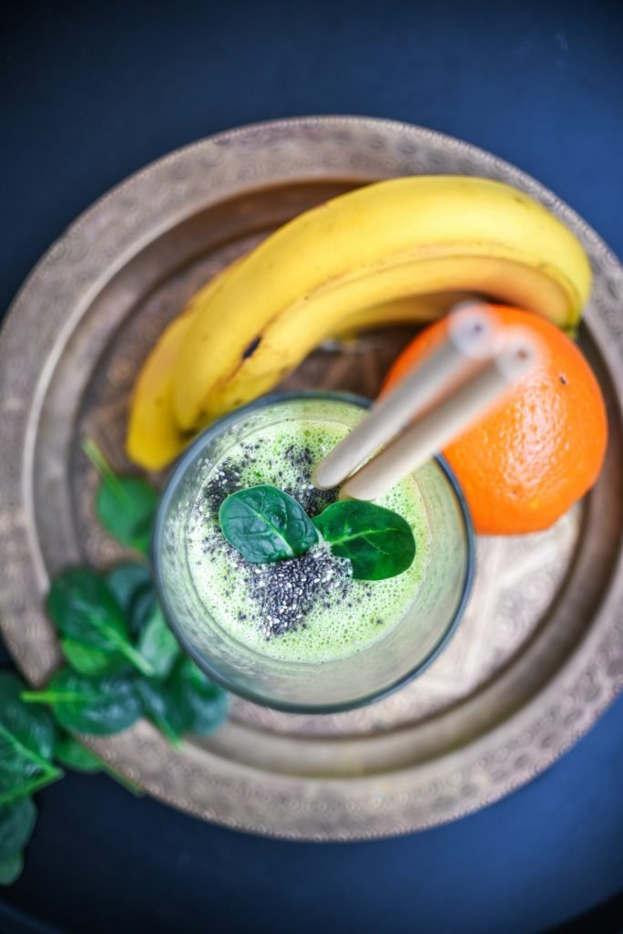 A glass of green smoothie with bananas and oranges
